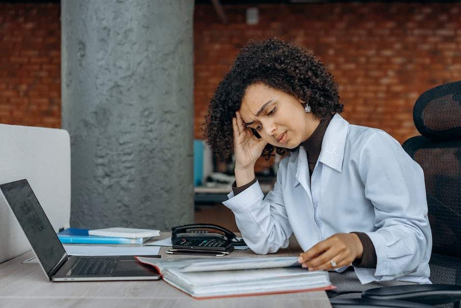 Image depicting a person sitting at a desk, looking stressed while holding tax documents in their hands.