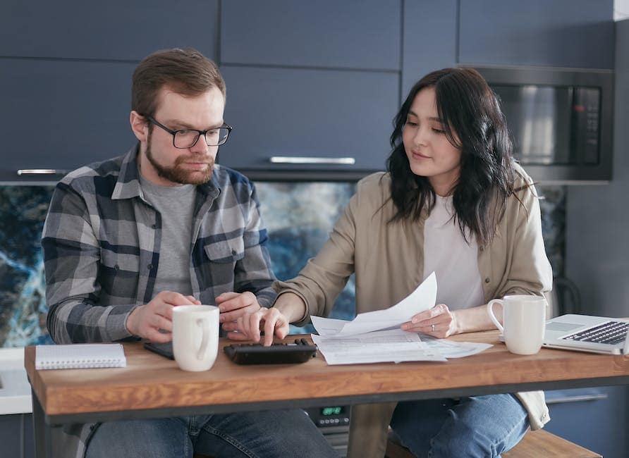 A person looking worried while surrounded by stacks of paperwork and a calculator.